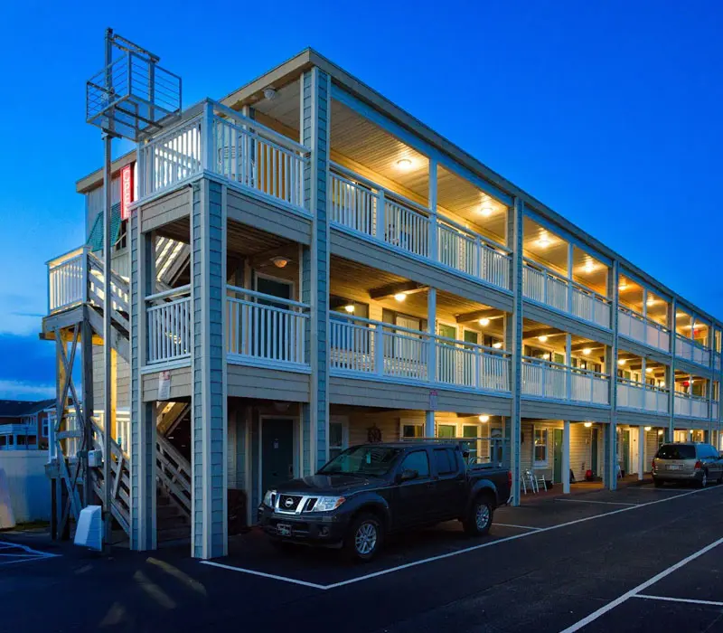 Seahorse Inn & Cottages at dusk, viewed from the parking lot, with its illuminated sign, exterior staircase and covered balconies lit against a deep blue sky
