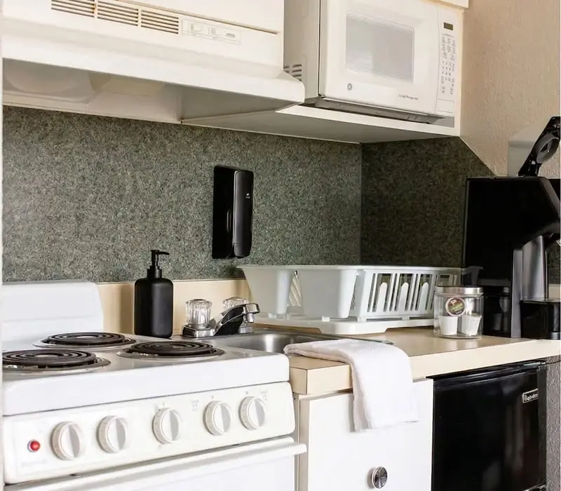A kitchenette with a white electric stove, a microwave, a sink and a black coffee maker
