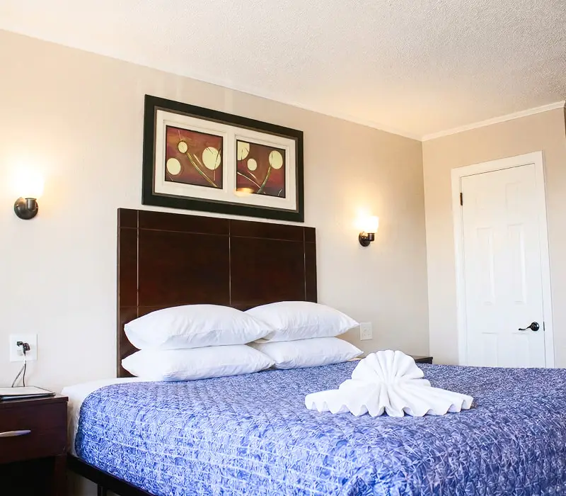 A king bed with a folded-towel display beneath a two-panel abstract print in a Deluxe Room at Seahorse Inn & Cottages