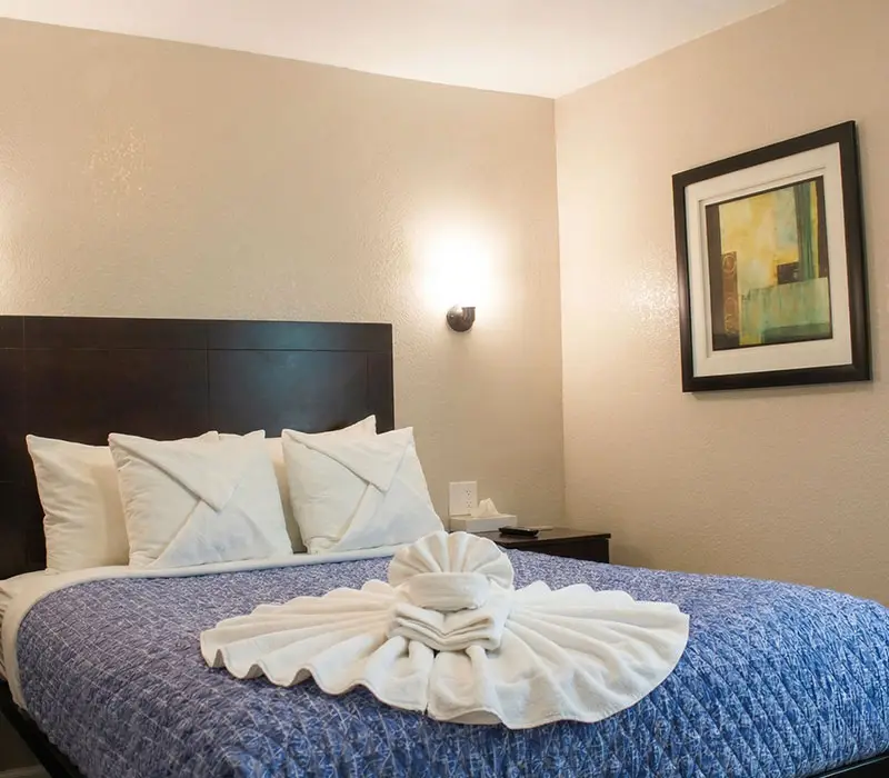 A queen bed with an elaborate fan-folded towel display beneath abstract art in a Deluxe Room at Seahorse Inn & Cottages