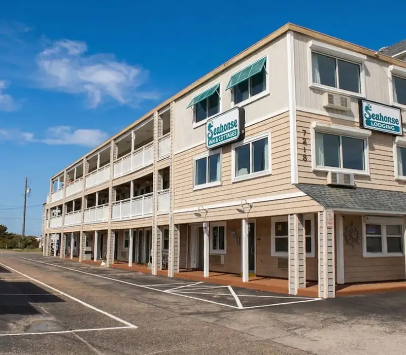 The exterior of a two-storey building with "Seahorse Inn & Cottages" and "Seahorse Lodging" signs, with an empty car park in the foreground
