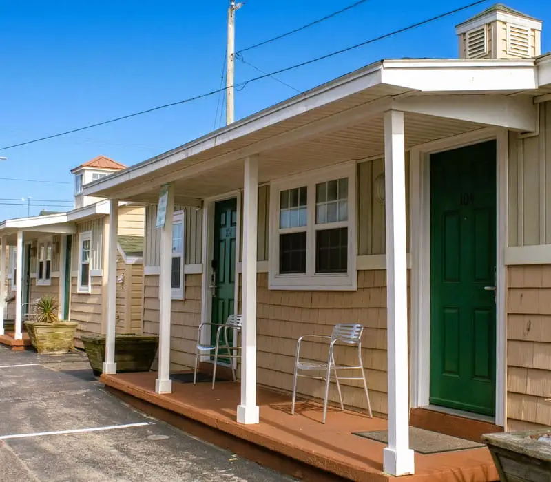 A row of single-storey motel rooms with light brown shingle siding, white porches and dark green doors