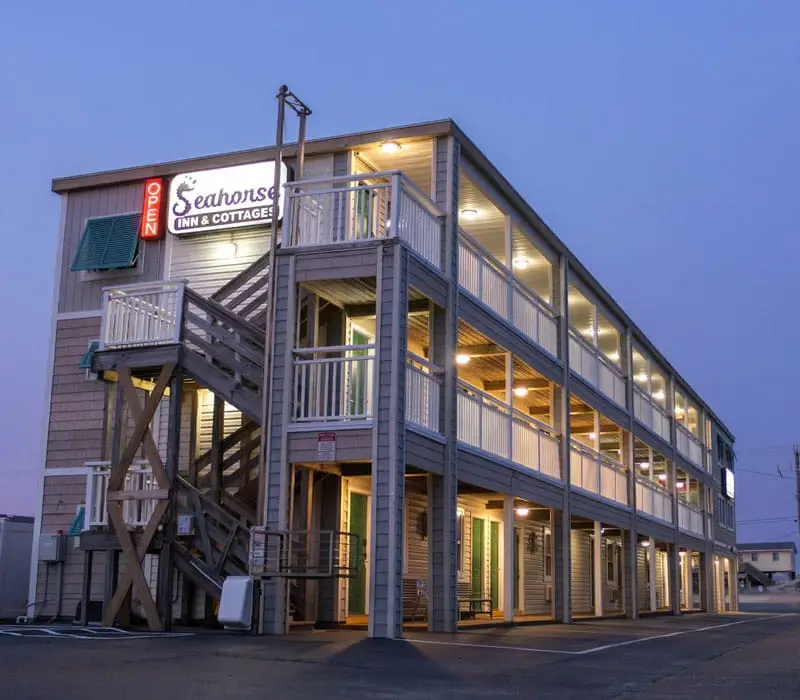 A two-storey building with an exterior wooden staircase and balconies, with a sign reading "Seahorse Inn & Cottages" and "OPEN" in red neon