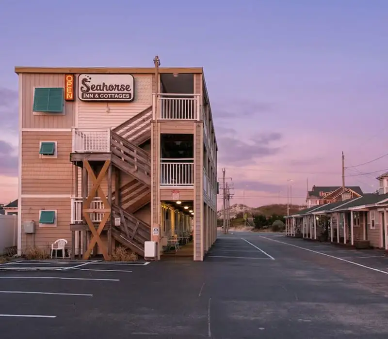 A three-storey building with an exterior wooden staircase and balconies, with a sign reading "Seahorse Inn & Cottages" and "OPEN"