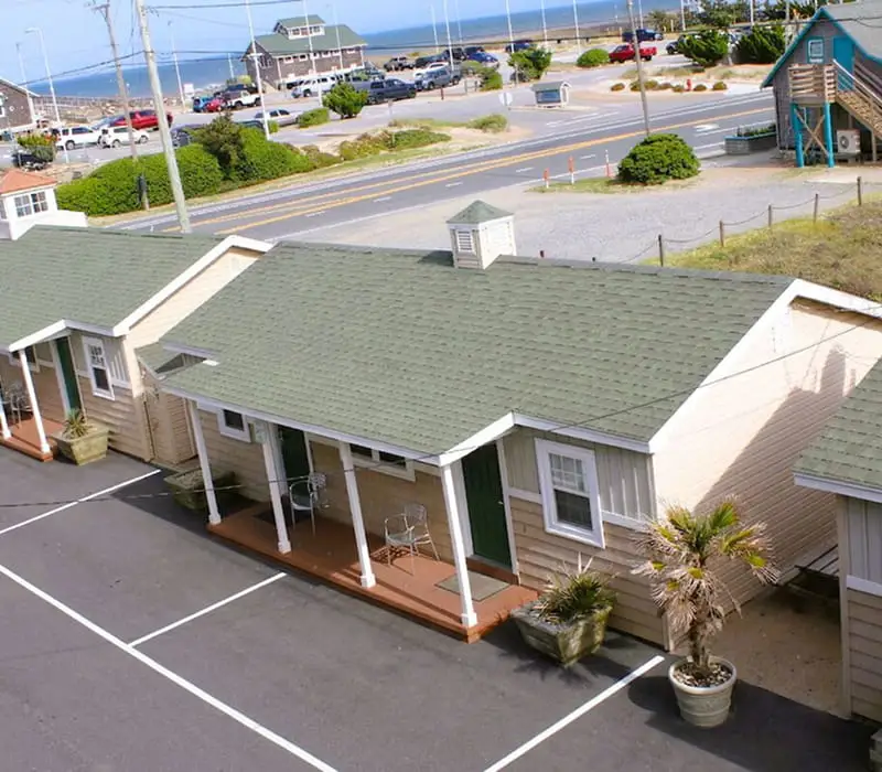 An aerial view of several single-storey buildings with green roofs and a car park, with a road and the ocean in the background