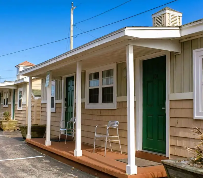 A row of single-storey motel rooms with light brown siding, white trim and green doors, under a clear blue sky