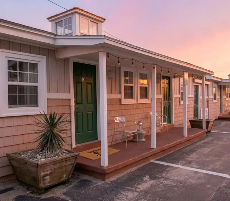 A row of single-storey motel rooms with green doors and small porches, under a pink and blue sky