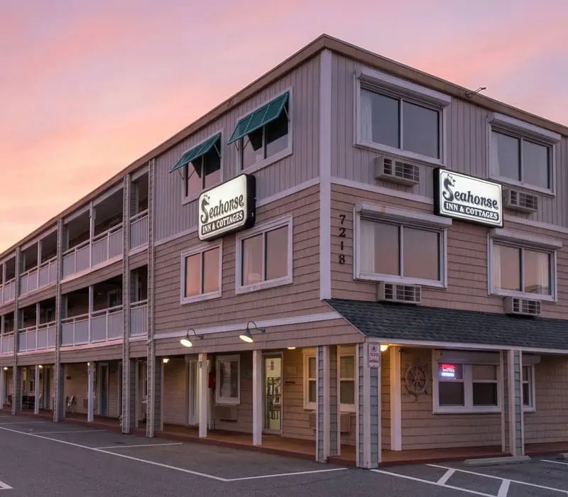 The two-storey Seahorse Inn & Cottages building with balconies and a car park in front, under a pink and orange sky