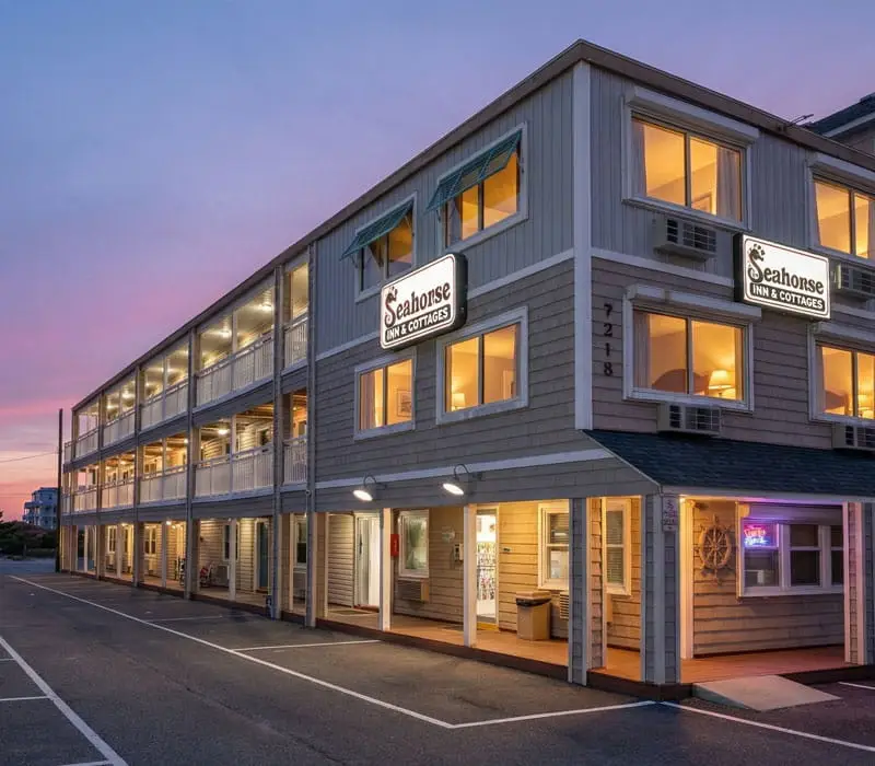 The three-storey hotel building with two "Seahorse INN & COTTAGES" signs, lit by the evening sky