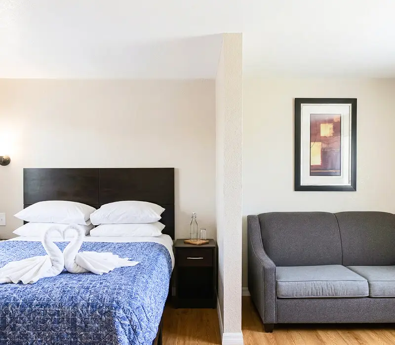 A queen bed with a folded-towel swan beside a grey sofa in a Premium Cottage sitting nook at Seahorse Inn & Cottages
