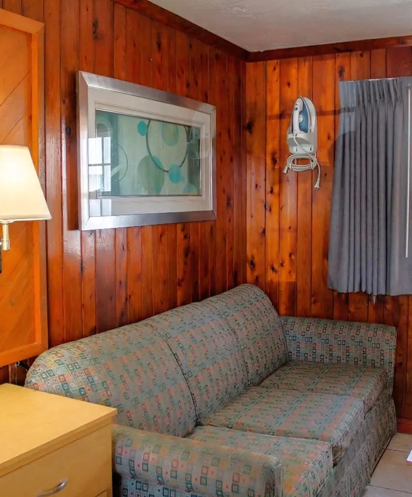 A wood-panelled sitting area with a patterned sofa bed, framed art and a wall-mounted iron in a Premium Cottage at Seahorse Inn & Cottages