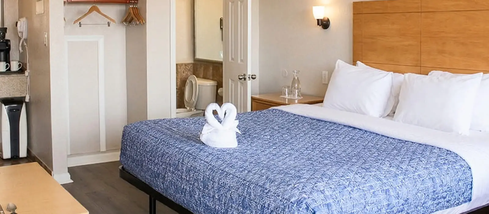 A guest room with a bed with blue quilted bedding, a wooden headboard, and a partial view of a bathroom