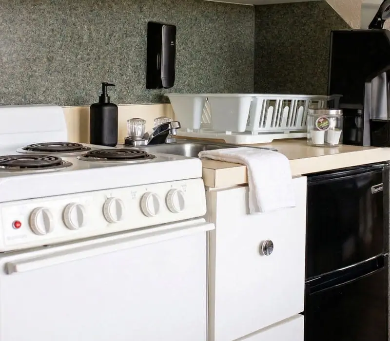 A kitchenette with a white electric stove, a sink, a dish drying rack and a black mini-fridge