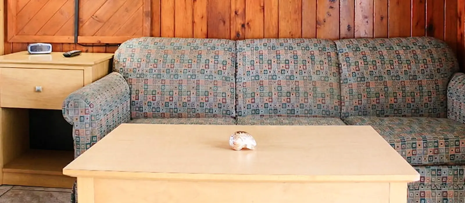 A patterned sofa sits in front of a wood-panelled wall, with a light wood coffee table and side table in the foreground