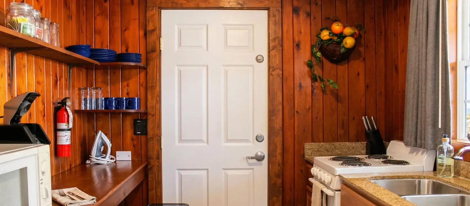 A kitchenette with wood-panelled walls, a white door, a microwave, a coffee maker, a fire extinguisher and a stove