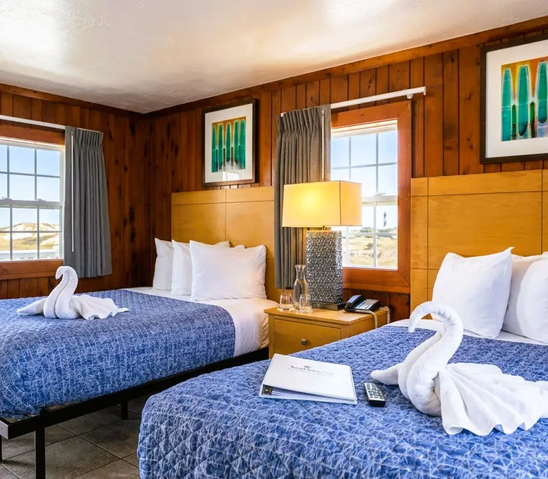 Two double beds with folded-towel swans in a wood-panelled Signature Cottage at Seahorse Inn & Cottages