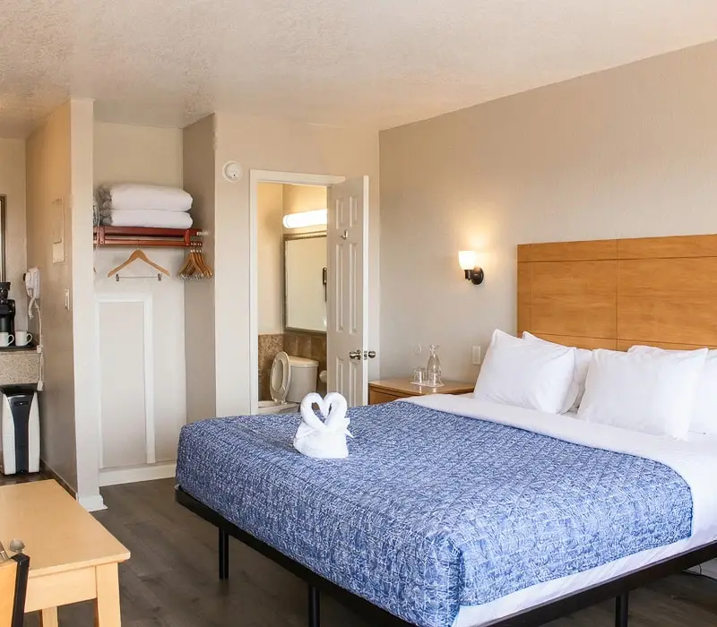 A king bed with a folded-towel swan beside an open closet and bathroom doorway in a Standard Room at Seahorse Inn & Cottages